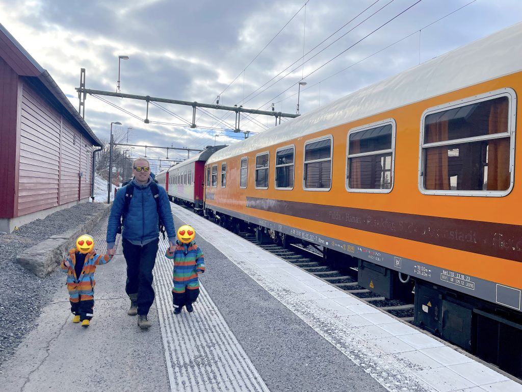 Two kids and a man on the platform next to a train. Photo. 