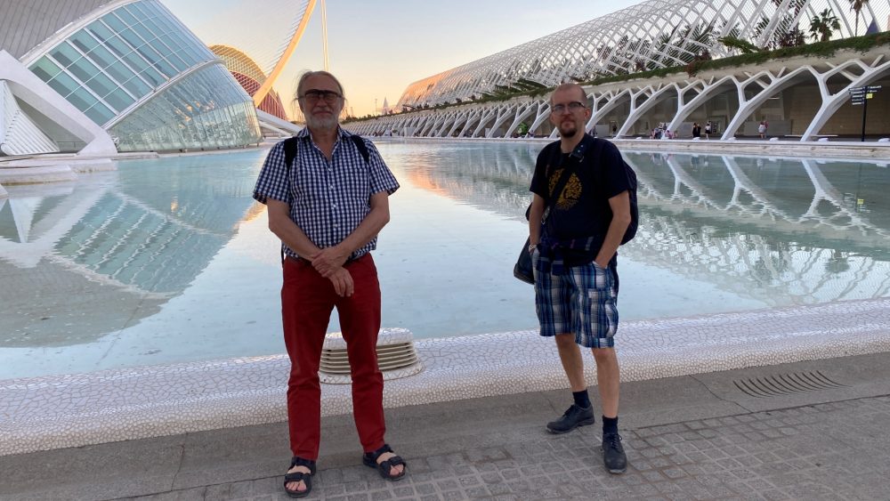 Two men in front of a contemporary architectural building. Photo.